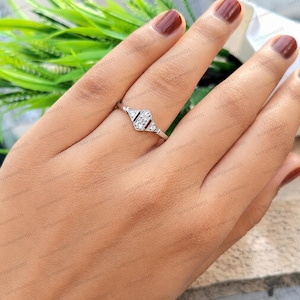 May include: A silver ring with a geometric design featuring three small diamonds. The ring has a thin band and a central diamond cluster, flanked by two triangular accents. The ring is shown on a person's finger.