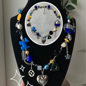May include: A beaded necklace with a variety of colorful beads, including blue, yellow, and clear glass beads. The necklace features charms, including a silver heart pendant, a star, and a black triangle. A smaller necklace is displayed in a circle.