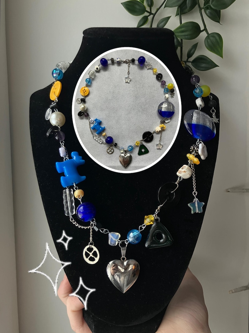 May include: A beaded necklace with a variety of colorful beads, including blue, yellow, and clear glass beads. The necklace features charms, including a silver heart pendant, a star, and a black triangle. A smaller necklace is displayed in a circle.
