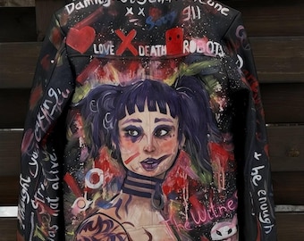 Könnte beinhalten: Schwarze Lederjacke mit handgemalten Kunstwerken. Die Jacke zeigt ein Porträt einer Frau mit lila Haaren und verschiedenen Phrasen und Symbolen, darunter "LOVE", "DEATH" und "ROBOTS".