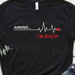 May include: Black t-shirt featuring the text "ANNNND... I'M BACK" and a heartbeat graphic. The image also shows blue jeans and brown sandals. The word "BLACK" is visible at the top left of the image.
