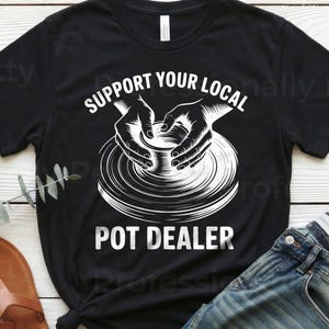 May include: Black t-shirt with the text "SUPPORT YOUR LOCAL POT DEALER" in white. The graphic shows hands shaping a pot on a pottery wheel. The shirt is paired with blue jeans and brown sandals.