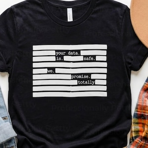 May include: Black t-shirt with white text: "your data is safe. we promise. totally." The shirt is shown with a denim jacket, a plaid shirt, and a brown hat. The text is arranged in a rectangular block.