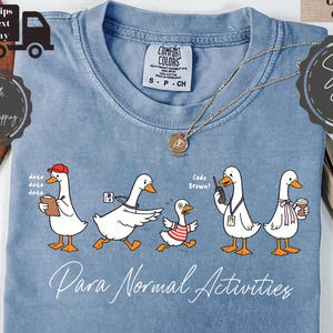 Puede incluir: Una camiseta color azul jean con un gráfico de cinco patos blancos en varios atuendos y poses. El texto "data data data", "Code Brown!" y "Para Normal Activities" está impreso en blanco. La camiseta tiene cuello redondo y una etiqueta Comfort Colors.