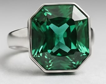 May include: A silver ring featuring a large, emerald-cut green gemstone. The gemstone is set in a silver bezel and has a faceted surface. The ring is displayed on a white surface with a black background.