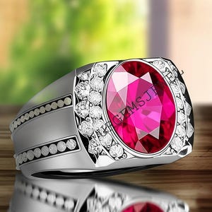 May include: A silver ring featuring a large, oval-cut, bright pink gemstone. The ring is embellished with smaller, clear gemstones around the main stone and along the band. The ring is displayed on a reflective surface.
