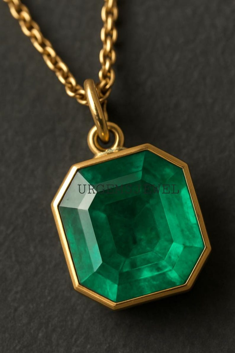 May include: A gold necklace with a large, emerald-cut green gemstone pendant. The pendant is set in a gold frame and hangs from a delicate gold chain. The text "URGE JEWEL" is visible on the pendant.