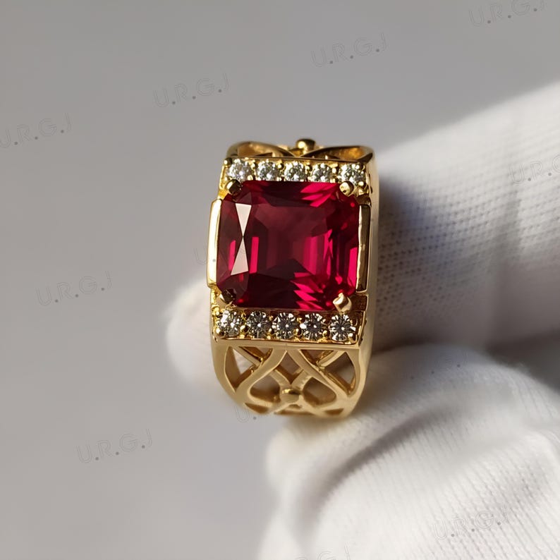 K&ouml;nnte beinhalten: Ein goldener Ring mit einem gro&szlig;en, rechteckigen, tiefroten Edelstein. Der Ring ist mit kleinen, klaren Edelsteinen und aufwendigen Filigranarbeiten am Band verziert. Ein auff&auml;lliges Schmuckst&uuml;ck.