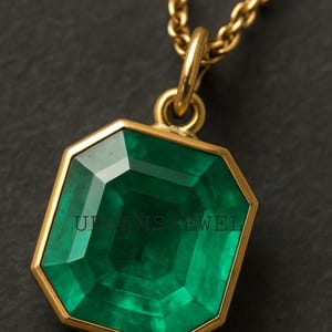 May include: A gold necklace with a large, emerald-cut green gemstone pendant. The pendant is set in a gold frame and hangs from a delicate gold chain. The text "U GEMS JEWEL" is visible on the pendant.