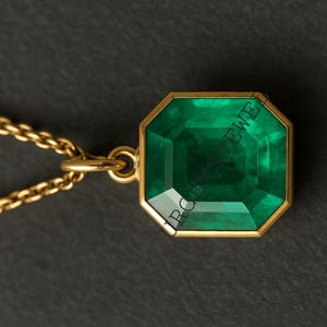May include: A gold pendant necklace featuring a large, emerald-cut, vivid green gemstone. The gemstone is set in a gold bezel and hangs from a delicate gold chain. The background is a dark gray.