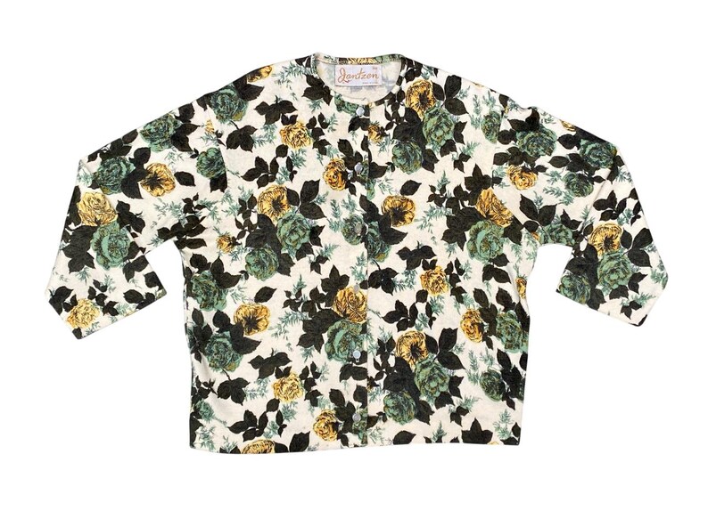 May include: A long-sleeved button-down cardigan featuring a cream-colored base with a dense floral print of dark green, muted teal, and golden yellow roses and leaves. The garment includes a round neckline and a vertical row of buttons.
