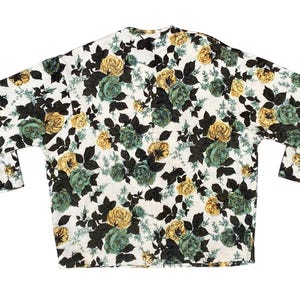May include: A long-sleeved shirt featuring a white base with a dense floral pattern of yellow and teal roses, accompanied by dark brown leaves and stems. The garment has a straight hemline and a simple neckline, showcasing a repeating botanical print.