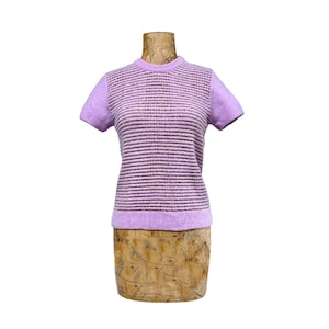 May include: A lilac-colored short-sleeved sweater with horizontal stripes in shades of purple and brown. The sweater is displayed on a wooden dress form. The sleeves and neckline are a solid lilac color.
