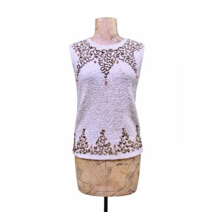 May include: A sleeveless, off-white top with intricate brown and orange beadwork. The beaded design adorns the neckline and hem, creating a decorative pattern. The top is displayed on a vintage dress form, showcasing its texture and detail.