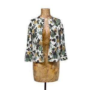 May include: A white, open-front jacket with a floral pattern of green, yellow, and black roses. The jacket has three-quarter sleeves and is displayed on a vintage dress form.
