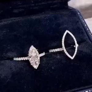 May include: Two diamond rings in a navy blue ring box. One ring features a marquise-cut diamond center stone, and the other has a marquise-shaped open design. The rings are set on a delicate band with small accent stones.