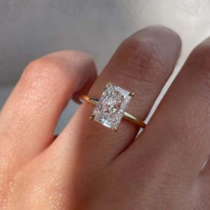 May include: A gold ring featuring a rectangular-cut diamond. The diamond has a brilliant sparkle. The ring's gold band complements the diamond's clarity. A timeless piece of jewellery, perfect for special occasions.