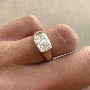 May include: A gold ring featuring a large, rectangular, clear gemstone. The ring is set in a gold band and is worn on a finger. The gemstone appears to be made of multiple smaller stones.