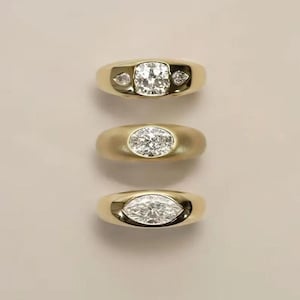 May include: Three gold rings with different diamond cuts. The top ring has a square-cut diamond with two smaller diamonds on either side. The middle ring features an oval-cut diamond, and the bottom ring has a marquise-cut diamond.