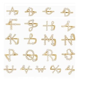 Pode incluir: Uma coleção de anéis dourados, cada um projetado em forma de uma letra do alfabeto. Os anéis são adornados com pequenas pedras preciosas brilhantes, criando um acessório glamouroso e personalizado. As letras são exibidas em uma grade.