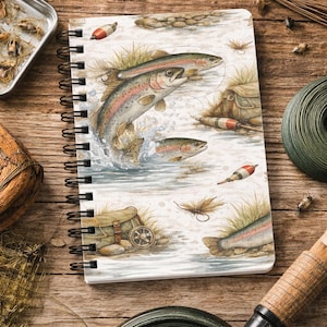 Puede incluir: Cuaderno espiral « Trout » de tamaño A5. La portada presenta una ilustración en acuarela de truchas saltando en un río, con aparejos de pesca. Tiene 150 páginas rayadas y una cubierta brillante y laminada.