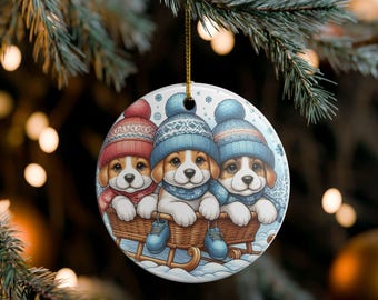 May include: Round Christmas ornament featuring three puppies in a sled. The puppies wear blue and red knit hats and scarves. The sled is brown, and the background is a snowy scene with snowflakes.