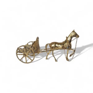 Puede incluir: Figurilla de metal dorado de un carro tirado por caballos. El carro tiene un diseño detallado con ruedas de radios y un asiento. El caballo está conectado al carro con una cadena. La figurilla está sobre un fondo blanco.