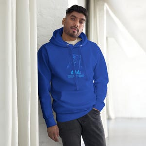 Puede incluir: Una sudadera con capucha azul real con un bolsillo delantero y una capucha con cordón. La sudadera presenta un gráfico azul claro de una figura encapuchada y el texto "4:14: SOUL FOUND". La persona de la imagen lleva la sudadera.