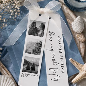 Könnte beinhalten: Ein weißes, rechteckiges Kartenetikett mit drei vertikal angeordneten, quadratischen Schwarz-Weiß-Fotos, dem Namen Sophia in Schreibschrift und dem schwarzen Text Will you be my MAID OF HONOR?, verziert mit einer transparenten weißen Schleife.