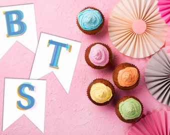 May include: A pink background with a banner that says "BTS" in colorful letters. There are six cupcakes with different colored frosting, and several paper fans in pink, peach, and gray.