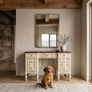 May include: A cream-colored wooden vanity desk with a dark brown top, featuring six drawers with small round knobs and decorative carved details. A rectangular mirror with a thin frame hangs above the desk, and a golden retriever puppy sits.