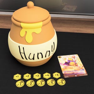 Pode incluir: Um pote de mel bege com tampa, apresentando um design de gota amarela e a palavra Hunny escrita em preto. Ao lado, há um cartão colecionável retangular com um urso amarelo e dez pequenas fichas amarelas numeradas de um a cinco.