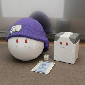 May include: A white and purple character-themed game set with a dice and a card. The set includes a white, egg-shaped figure with red eyes and a purple hat, and a white and gray box.
