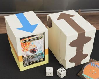 May include: Two white card storage boxes with blue and brown arrow designs. One box is open, revealing a card with a colorful illustration. Two white dice and a Magic card are also present. The boxes are on a black surface.