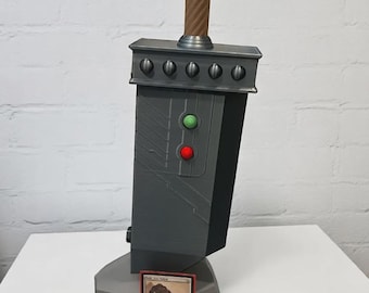 May include: A large, gray replica sword with a brown handle and a rectangular hilt featuring six circular details. The sword has green and red circular details. A trading card is at the base of the sword.