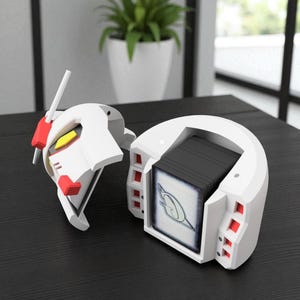 May include: A white and red Gundam-themed card holder, open to reveal a stack of cards. The holder has a detailed design with red accents and yellow details. The cards inside have a blue and white design.