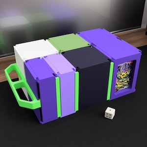 Könnte beinhalten: Eine modulare Aufbewahrungsbox in Lila, Schwarz, Weiß und Grün mit einem grünen Griff. Die Box ist in Abschnitte unterteilt und enthält eine Kartenanzeige. Ein weißer Würfel mit schwarzen Punkten liegt daneben.