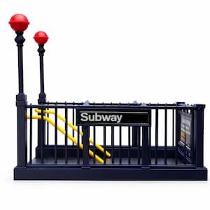 May include: A miniature replica of a subway entrance, featuring a dark blue metal frame with yellow handrails and a sign that reads "Subway." Two red globe lights top the black posts. The design is reminiscent of a classic city subway.