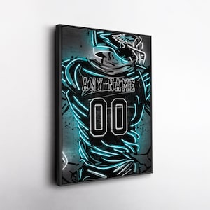May include: Framed artwork featuring a football player in a neon-style design. The player's jersey displays "ANY NAME" above the number "00" in white. The artwork has a black frame and a dark background with teal neon accents.