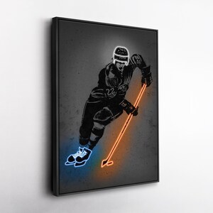 May include: Black framed wall art featuring a hockey player in action. The player is depicted in silhouette with neon blue skates and a neon orange hockey stick. The helmet has the word "JOFA" on it. The background is a textured gray.