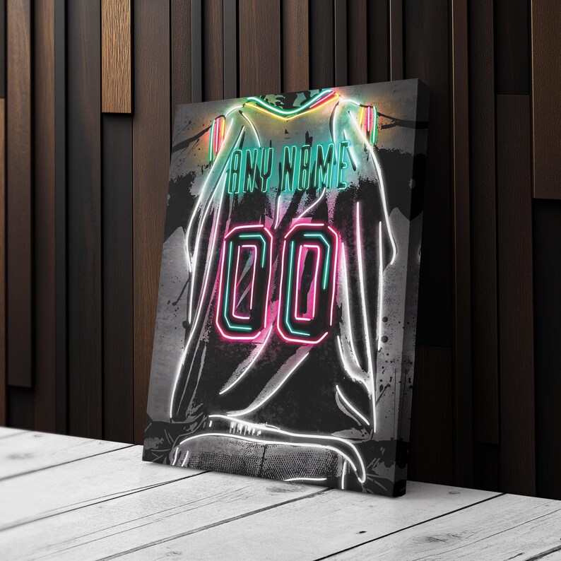Op de afbeelding: Canvas print van een neon-stijl jersey met de tekst "ANY NAME" boven het nummer "00". Het jersey-ontwerp heeft een zwarte achtergrond met witte contouren en spetters van kleuren, waaronder groen en roze.