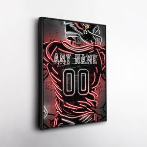 May include: A framed neon-style artwork of a football player in a jersey with the text "ANY NAME" above the number "00". The artwork features red and white neon lines on a dark background, creating a striking visual effect.