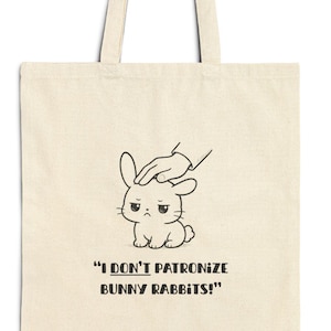 Puede incluir: Bolso tote de lona beige con un dibujo lineal negro de un conejito siendo acariciado en la cabeza. El texto "I DON'T PATRONIZE BUNNY RABBITS!" está impreso debajo de la ilustración del conejo. El bolso tiene dos asas largas.