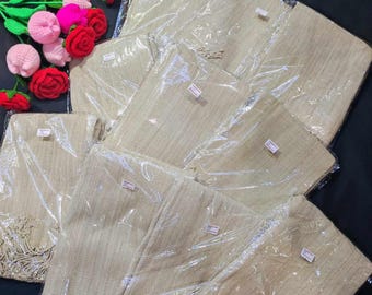 May include: A collection of beige shawls, each individually wrapped in clear plastic. The shawls have a fringed edge and are stacked together. Crochet flowers in pink, red, and green are in the upper left corner.