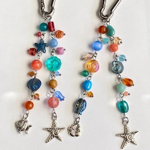 Peut inclure: Deux porte-clés perlés avec des mousquetons argentés. Chaque porte-clés présente un assortiment coloré de perles de différentes formes et tailles, notamment des étoiles, des poissons et des breloques en forme de fleurs. Les perles sont dans les tons de bleu, orange, rose et vert.