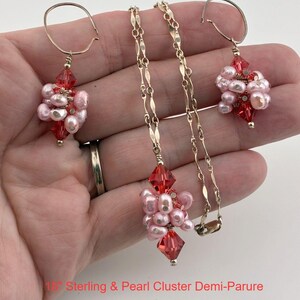 May include: A jewelry set featuring a necklace and two earrings, each with clusters of light pink pearls and faceted red crystals on gold-toned metal. The necklace chain is 18 inches long. The text 18" Sterling & Pearl Cluster Demi-Parure is visible.