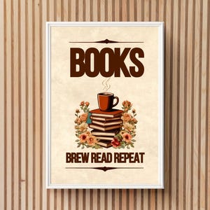 以下が含まれることがあります： 上部に「BOOKS」、下部に「BREW READ REPEAT」と書かれた額入りのアートプリント。画像には、コーヒーカップが上に置かれた本の山と、それを囲む花が描かれています。プリントは白いフレームに入っています。