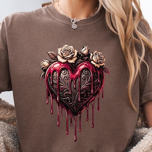 Puede incluir: Camiseta marrón con un diseño de corazón con un acabado rojo brillante y detalles de filigrana negra. Rosas y hojas color crema adornan la parte superior del corazón. Prenda de vestir informal y cómoda.