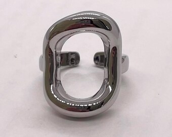 May include: A silver-colored ring with a large, open oval design. The ring has a thick, rounded band that wraps around the finger, with an adjustable opening. The ring is made of a shiny, polished metal.