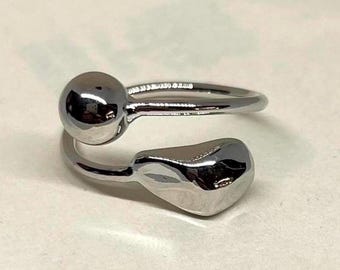 May include: A silver-colored ring with a unique design. The ring features a spherical shape on one end and a teardrop shape on the other, connected by a smooth, curved band. The ring is made of a shiny, reflective metal.